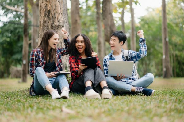 three-young-college-students-is-reading-a-book-while-relaxing-sitting-on-grass-in-a-campus-park.jpg